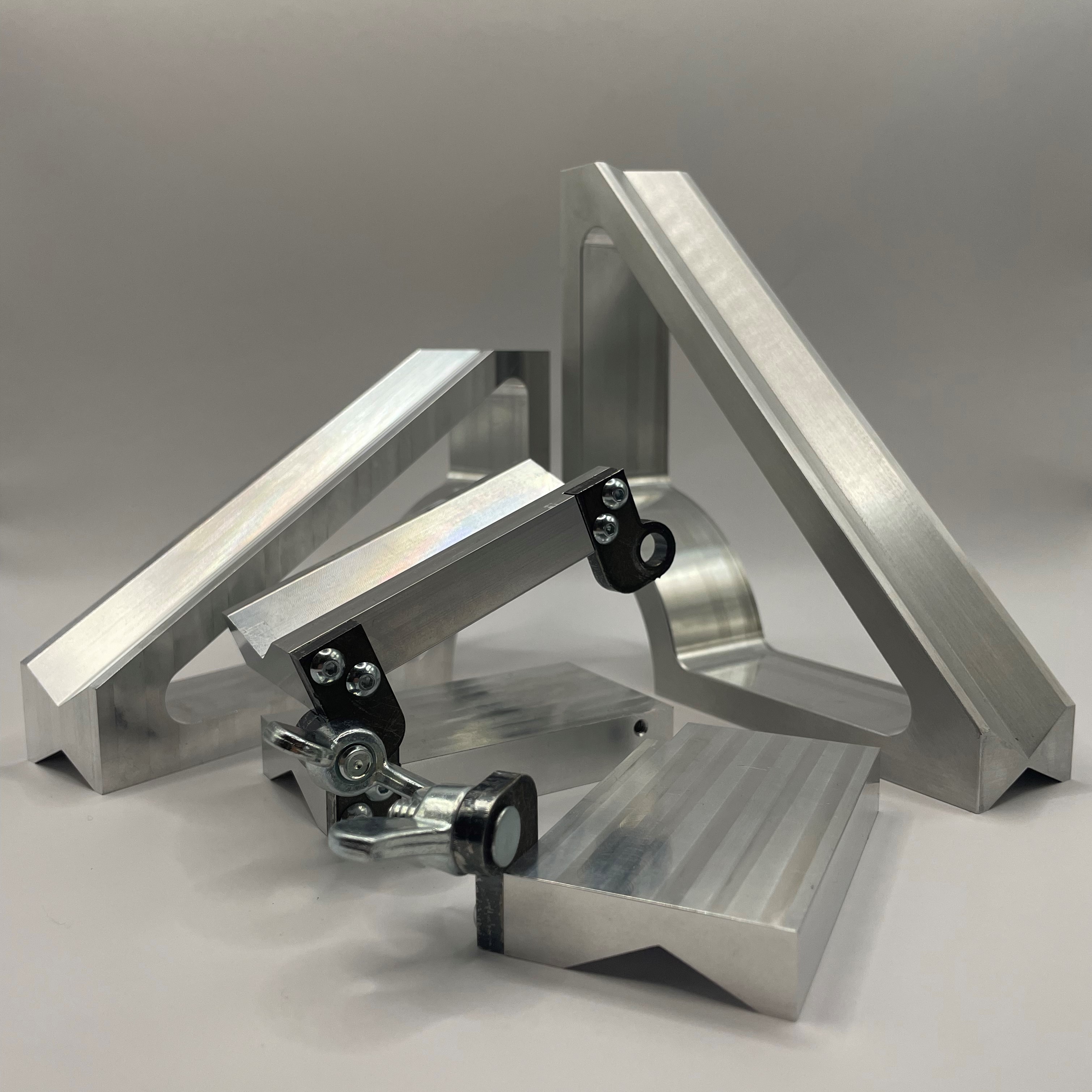 Multiple custom machined aluminum fixtures laid out on a gray background